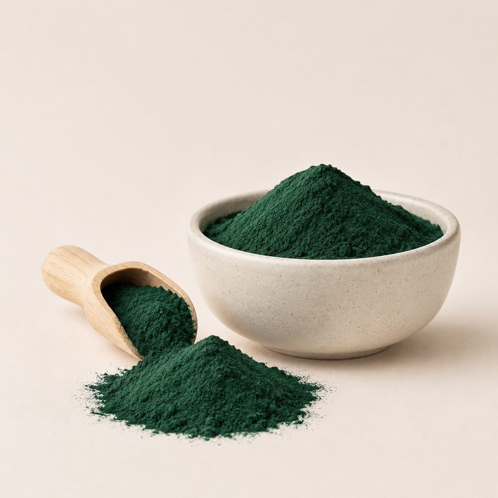 tamsiai žali spirulinos milteliai keraminiame dubenėlyje ir mediniame semtuvėlyje